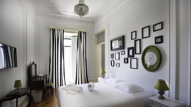 Une chambre d’hôtel avec un grand lit, un bureau avec une lampe, une chaise, une petite table avec une lampe, et un mur orné de tableaux encadrés et d’une assiette verte.