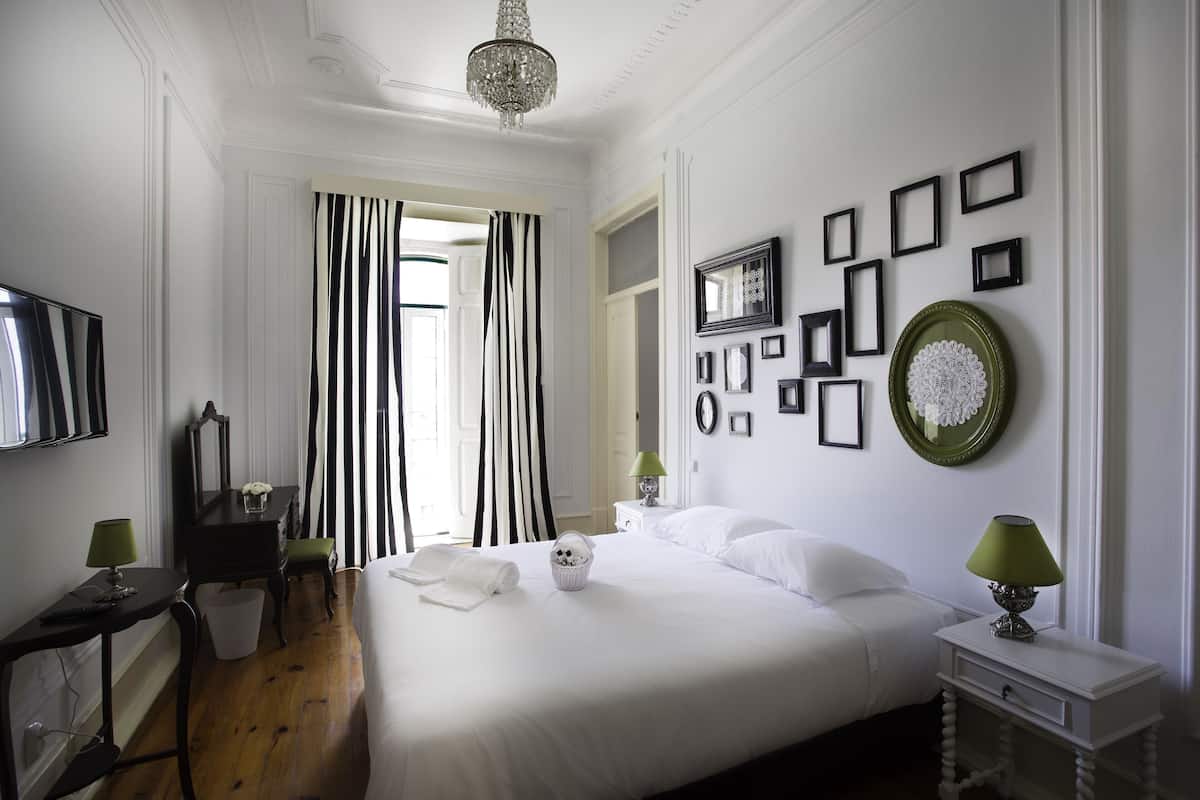 Habitación de hotel con una cama grande, un escritorio con lámpara, una silla, una mesita con lámpara y una pared con cuadros y un plato verde.