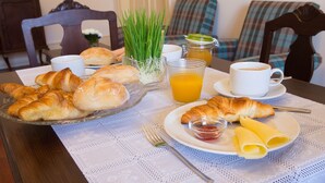 Une table dressée pour le petit-déjeuner, avec des croissants, du jus de fruits et du café, recouverte d’une nappe en dentelle.