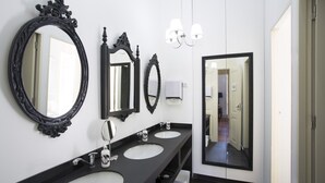 Une salle de bain moderne avec trois vasques, des miroirs noirs à motifs décoratifs et un lustre.