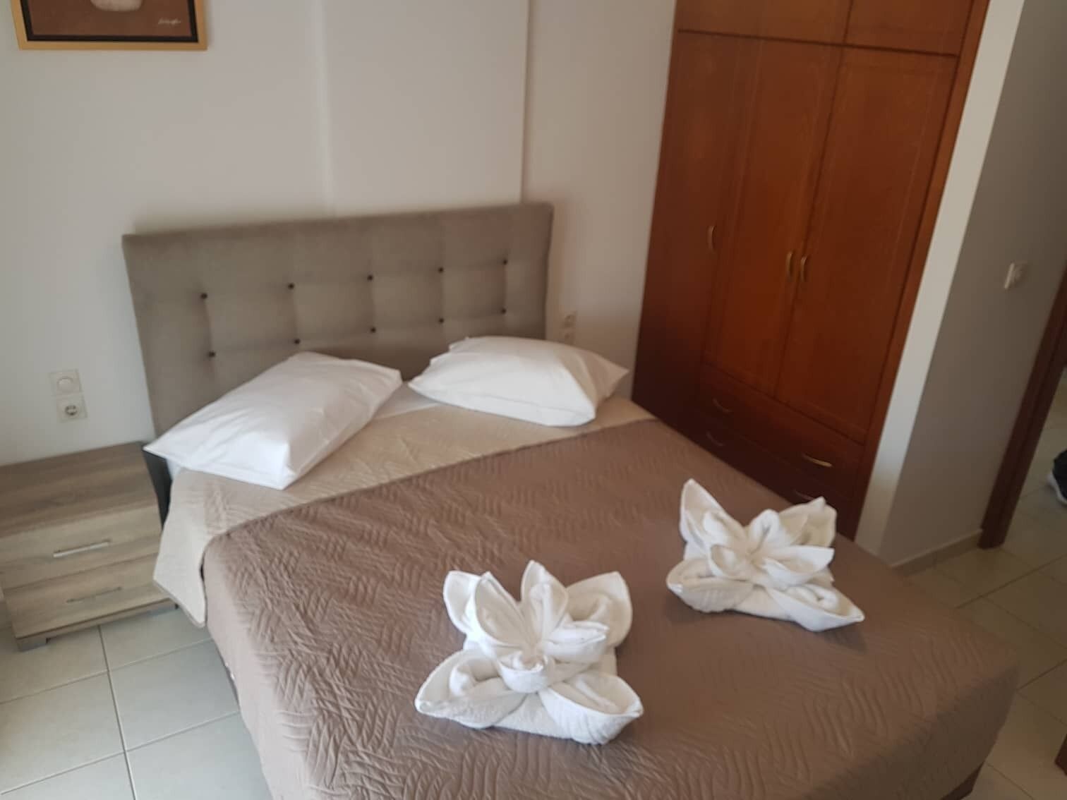 A hotel room with a bed, a wooden wardrobe, and a tiled floor.
