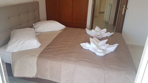 A neatly made bed with a beige quilt, two pillows, and two towels arranged in a lotus shape on the bed. - Ria's Sea View Apartment (Chania)