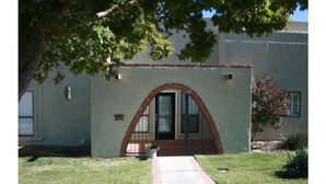 Un edificio con un arco de ladrillo en la entrada, un pequeño jardín y un camino pavimentado que conduce al acceso.