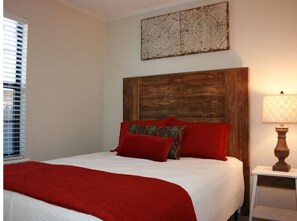 Ein Schlafzimmer mit einem Holzkopfteil, einer weißen Bettdecke und roten Kissen.