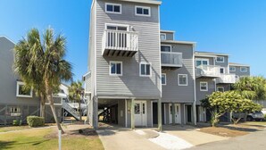 A multi-story residential building with balconies, a covered entrance, and a palm tree in the foreground.