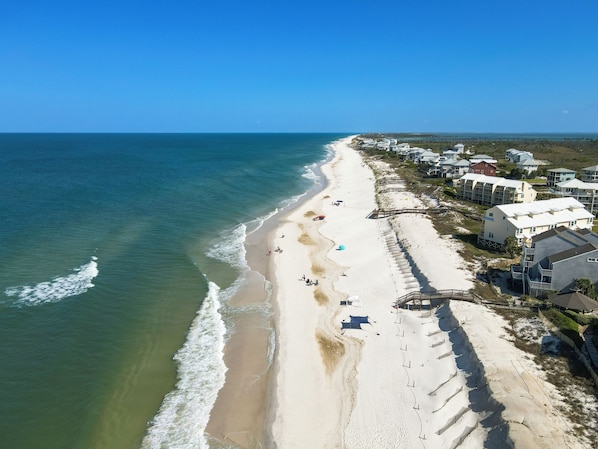 An aerial view of a beach with houses along the shore, a clear sky, and the ocean.