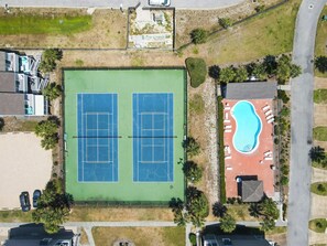 Ein Luftbild eines Anwesens mit zwei Tennisplätzen, einem Schwimmbad und umliegender Grünfläche.