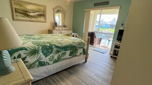 Ein Schlafzimmer mit Bett, Nachttisch, Deckenventilator und Blick auf ein Schwimmbad durch eine Schiebetür.