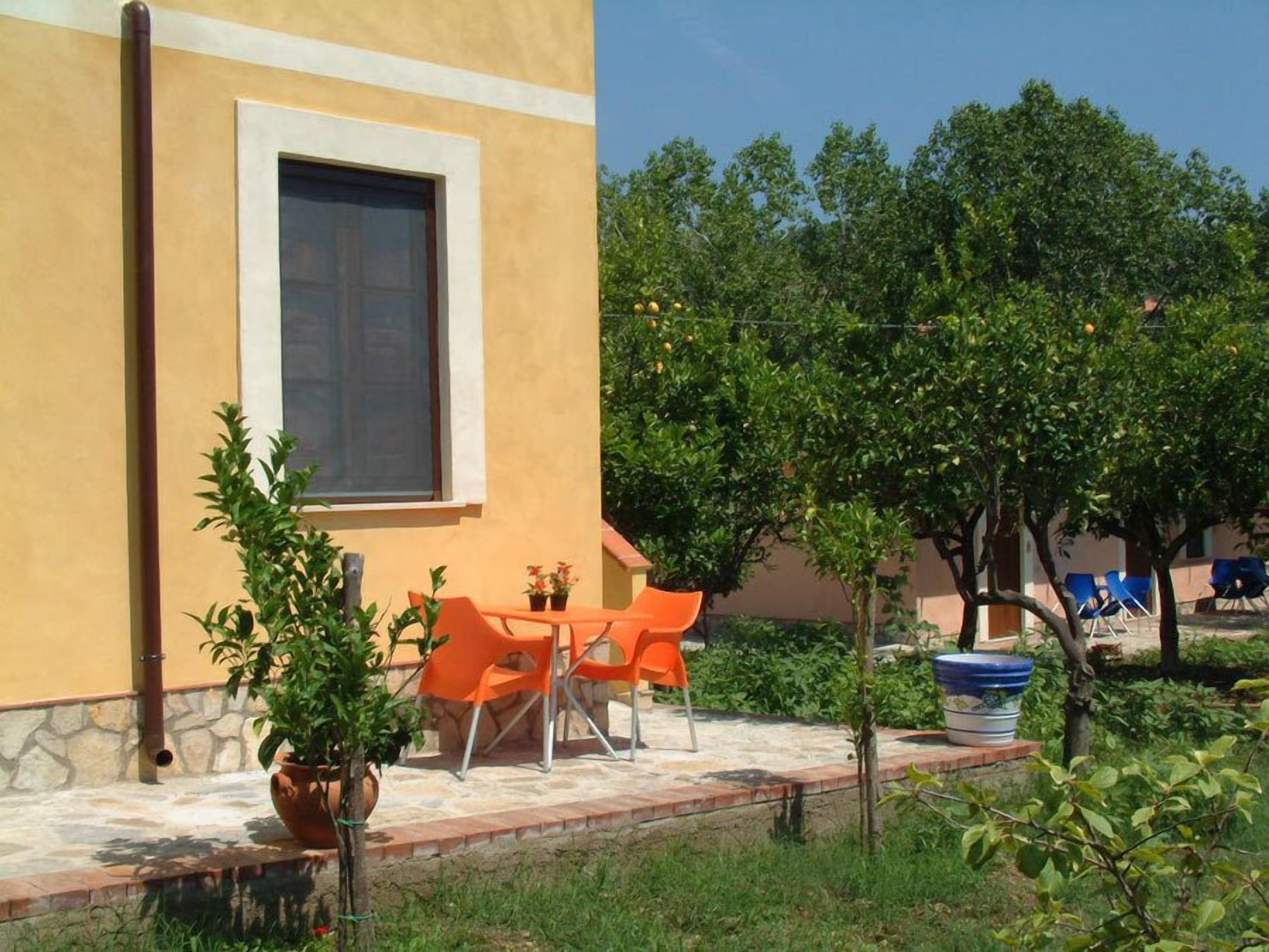 A building with a large window, outdoor seating, and a garden with trees and chairs.