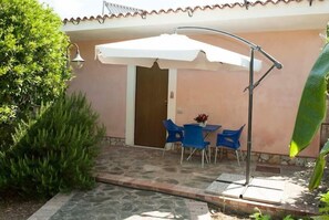 A patio area with a table and chairs under a white umbrella, surrounded by greenery and a stone floor. - Nel Giardino Dei Limoni (Montecorice)