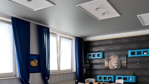 Ein modernes Schlafzimmer mit Bett, Schreibtisch und Stuhl. Ein Fenster mit Vorhängen, eine Heizung und eine Wand mit einem Bild sind zu sehen.