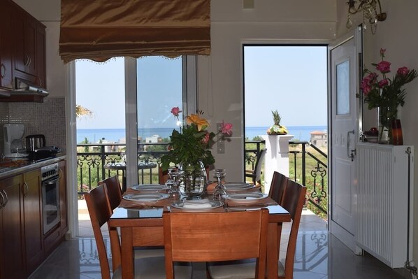 A dining area with a view of the sea, a kitchen with wooden cabinets, and a balcony with a railing.