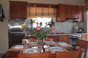 A dining area with a wooden table set for four, surrounded by wooden cabinets and a stainless steel refrigerator.