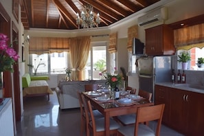 A dining area with a wooden table set for four, a sofa, and a kitchen with wooden cabinets and a refrigerator.