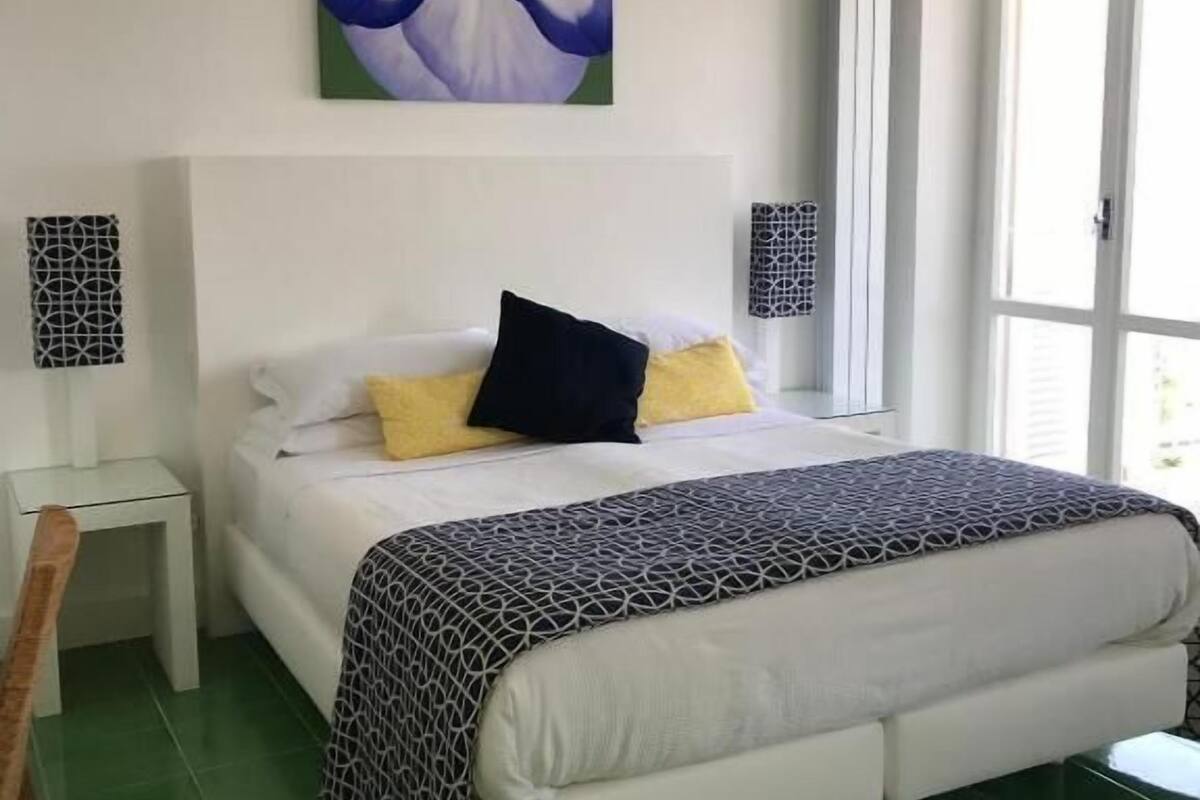 Une chambre à coucher avec un lit, une table de chevet, une chaise, une fenêtre et un tableau au mur.