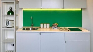 Eine kompakte Küche mit weißen Schränken, einer grünen Spritzschutzwand und einem Spülbecken.