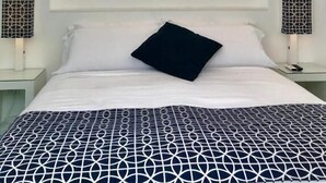 Ein Schlafzimmer mit einem Bett, einem an der Wand hängenden Meeresblick-Gemälde und zwei Nachttischlampen.