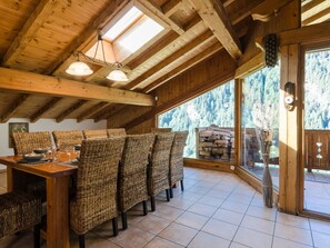 A wooden dining area with wicker chairs, a wooden table, and a view of a forest through large windows.