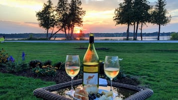Eine Weinflasche, zwei Gläser und ein Teller mit Essen auf einem Tisch im Freien mit Blick auf den Sonnenuntergang.