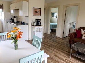 A compact living space with a kitchenette, a dining area with a table and chairs, a sofa, and a bed in the adjacent room. - #17 Isle View - Fishing, Sunsets, Beaches, Golfing (Alburg)