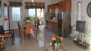 A modern kitchen with wooden cabinets, a refrigerator, and a dining area with a table and chairs. - Zoi's Holidays Apartment (Platanias)