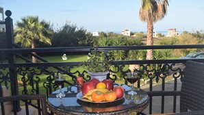 A table with a fruit bowl, wine glasses, and a potted plant on a balcony overlooking a garden and the sea. - Zoi's Holidays Apartment (Platanias)