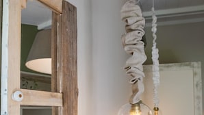 A rustic room with a wooden-framed mirror, a hanging light fixture with a glass enclosure, and a bed with pillows and bags. - Le Clos des Bourges (Le Rouret)