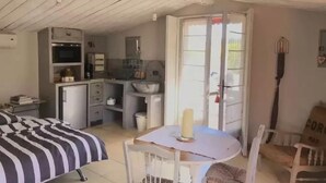 A compact room with a bed, a small table, a chair, a kitchenette, and a door leading outside. - Le Clos des Bourges (Le Rouret)