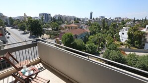 A balcony with a table and chairs, overlooking a cityscape with buildings and trees. - The Bridge-House Apartment (Nicosia)
