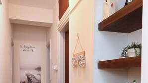 A hallway with wooden flooring, a welcome sign, a framed photo, a plant, and a shelf with books. - The Bridge-House Apartment (Nicosia)