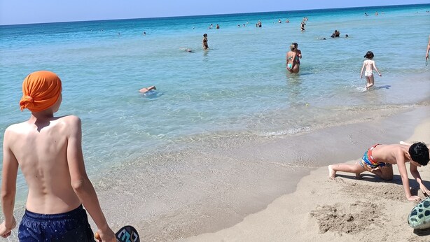 A beach scene with clear skies and people swimming and sunbathing. - A few steps from the crystal clear sea of Puglia (Lido Marini)
