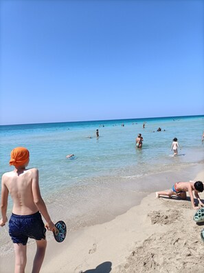 Una spiaggia con cielo sereno e persone che nuotano e prendono il sole.