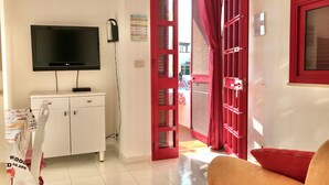 A room with a TV mounted on the wall, a white cabinet, a red door, and a sofa. - A few steps from the crystal clear sea of Puglia (Lido Marini)