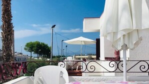 An outdoor seating area with white umbrellas and chairs, overlooking a clear blue sky and a building with a red roof. - A few steps from the crystal clear sea of Puglia (Lido Marini)