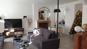 A living room with a sofa, TV, fireplace, Christmas tree, and a dining area with a table and chairs.