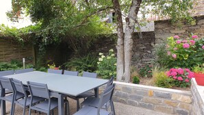 An outdoor patio with a table and chairs, surrounded by lush greenery and flowering plants.