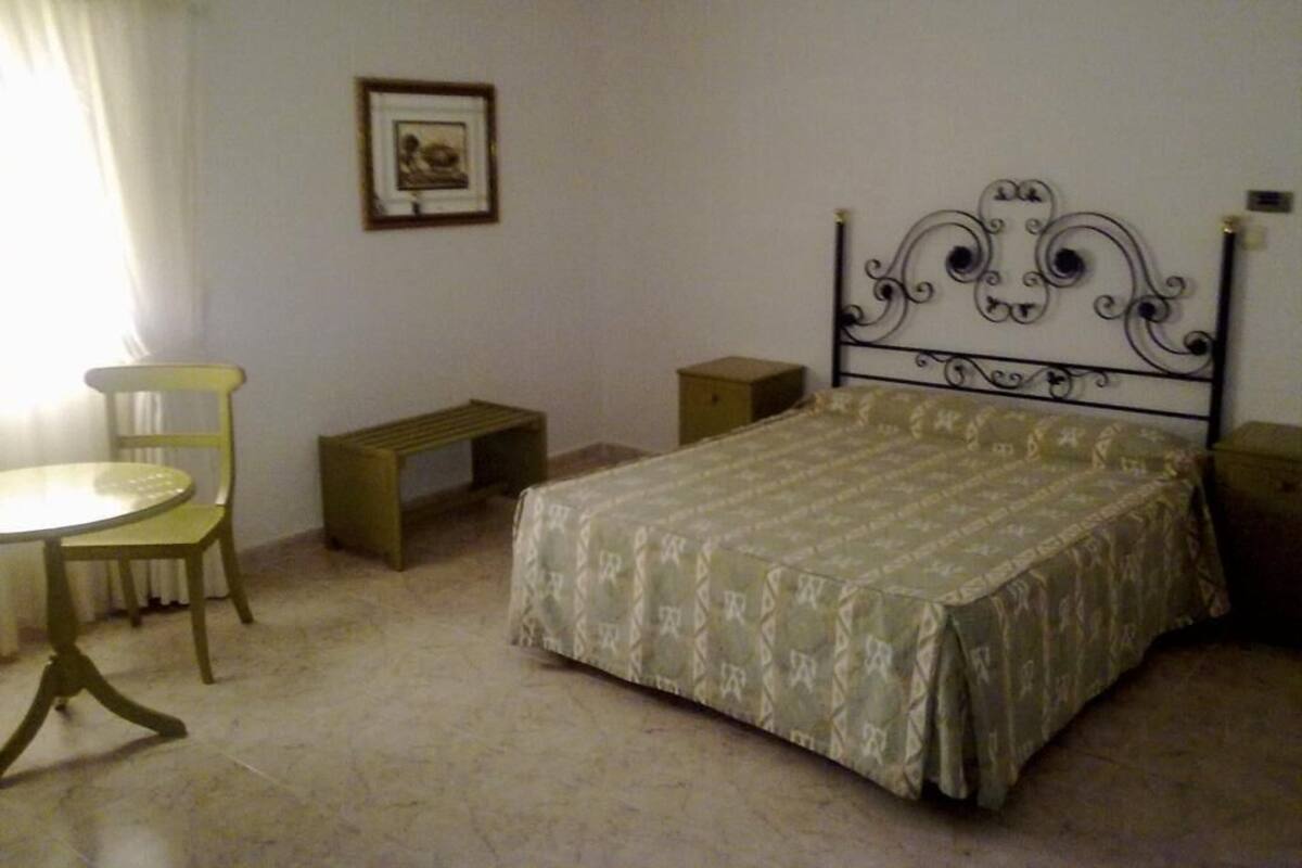 A bedroom with a bed, a chair, a small table, and a bench.
