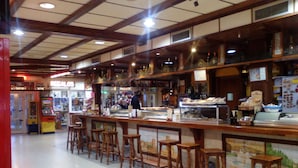 Una zona de bar con taburetes de madera, una barra con vitrina y suelo de baldosas.