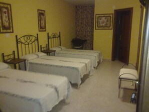 Una habitación con cuatro camas alineadas, una silla, una mesita y una puerta.