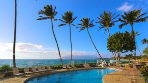 A poolside area with lounge chairs, palm trees, and a view of the ocean. - Chic and Remodeled Royal Mauian Beachfront  | Ground Floor Oceanfront Living (Kihei)