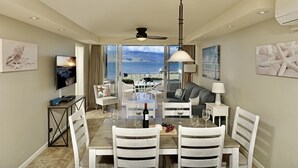 A dining area with a view of the ocean, white furniture, and a television on the left. - Chic and Remodeled Royal Mauian Beachfront  | Ground Floor Oceanfront Living (Kihei)