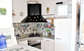Kitchen features a central gas stove, oven, and range hood, along with a tiled backsplash and ample countertop space.