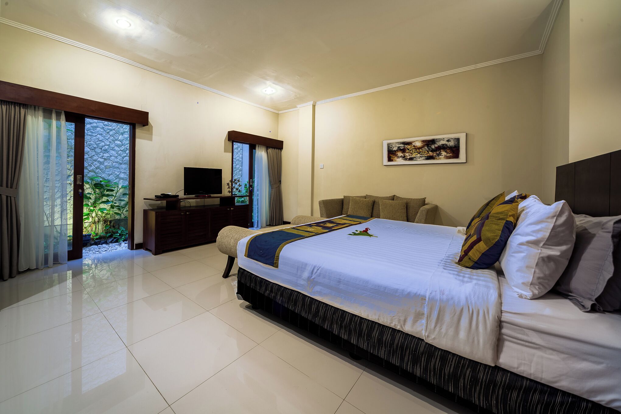 Habitación de hotel con una cama grande, televisión, escritorio y vista a zonas verdes por la ventana.