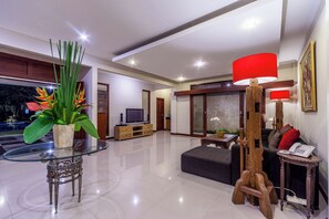 A modern living room with a glass table, a wooden sculpture, a red lamp, and a sofa.