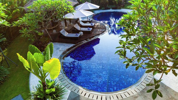 Ein kreisförmiger Infinity-Pool mit Liegestühlen und Sonnenschirmen, umgeben von üppiger Vegetation und einer strohgedeckten Struktur.