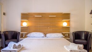 A hotel room with a large bed, two bedside lamps, a wooden headboard, and two leather armchairs.