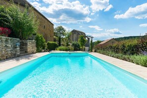 Una piscina rectangular de aguas cristalinas y color azul, rodeada de muros de piedra y abundante vegetación.