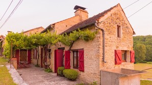 Ein Steinhaus mit roten Fensterläden und einer mit Weinreben bewachsenen Mauer.