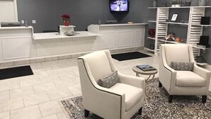 A modern reception area with a flat-screen TV, white reception desk, and two armchairs with patterned cushions. - Belamere Swimming Pool Suites (Cumming)