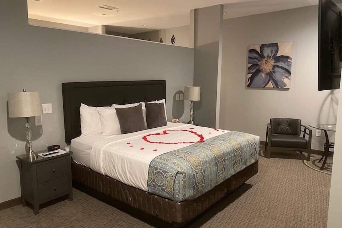 Une chambre d’hôtel avec un grand lit, deux tables de chevet, une chaise, un téléviseur et un tableau au mur.